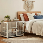 OnePaw Ares white metal pet crate next to a bed with pillows in a bedroom setting