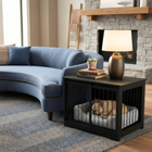 OnePaw AURELIA dog lying in a black pet crate next to a blue sofa in a living room.