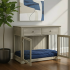 OnePaw LYRA wooden pet crate with blue bedding in a room with a plant and abstract art on the wall.