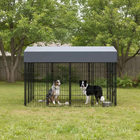 Two dogs inside a large outdoor dog kennel with a gray roof in a grassy area.